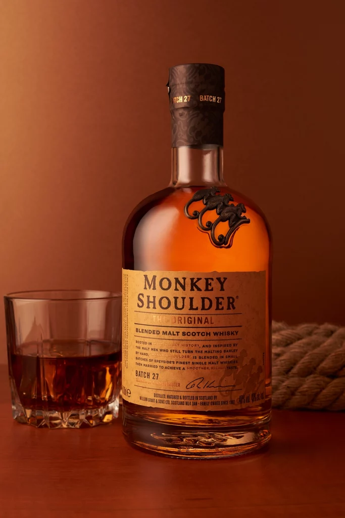 Photographie d'une bouteille de whisky avec un verre à whisky rempli, tons chauds orangés, ambiance bar - Photographe publicitaire boissons spiritueux - photographe e-commerce - photographe de produits - Aurore Aivrest
