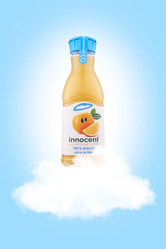 Photographie d'une bouteille de jus d'orange sur un nuage et un fond bleu ciel avec un halo lumineux - Photographe publicitaire boissons - photographe e-commerce - photographe commercial - Aurore Aivrest