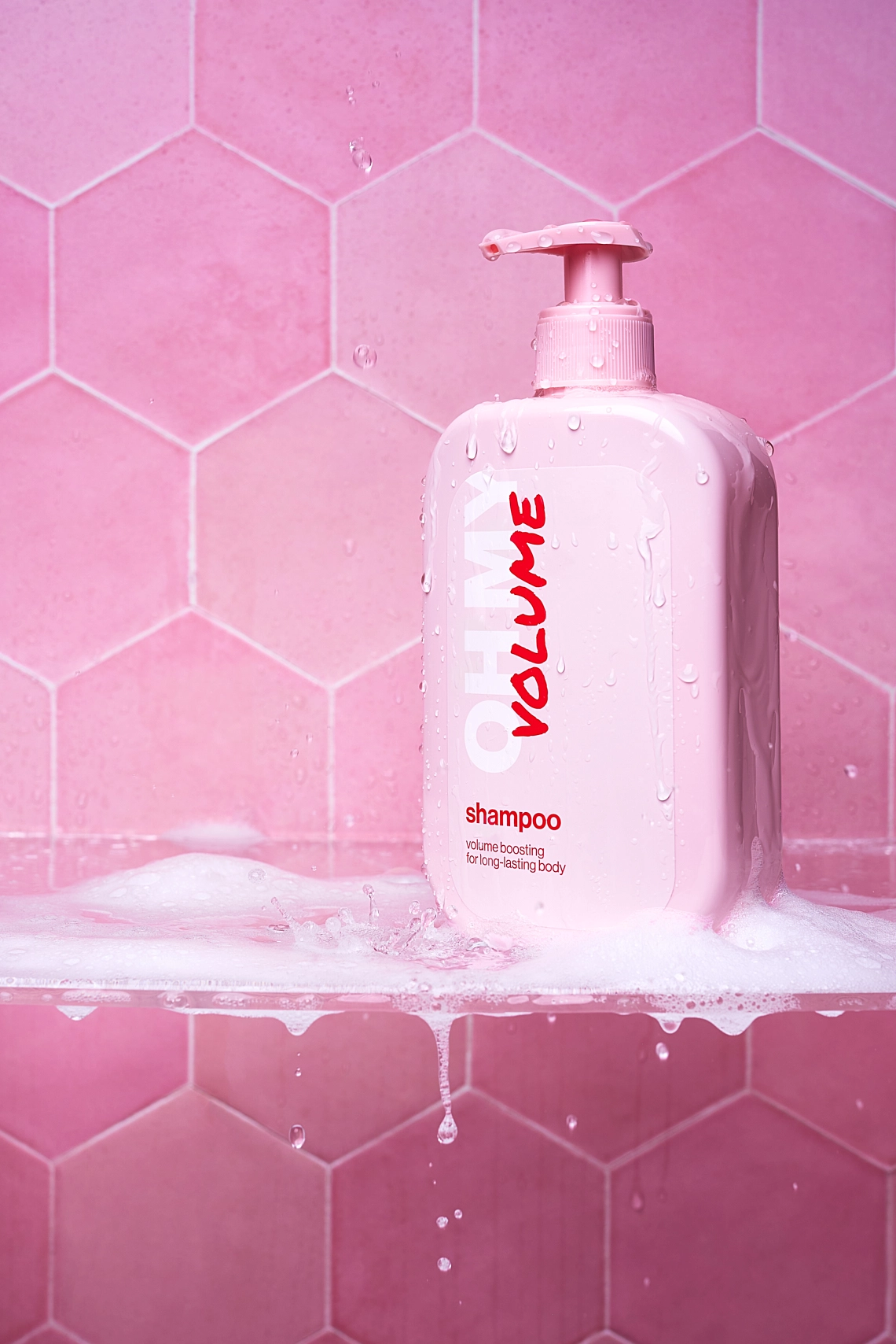 Photographie d'une bouteille rose pale de shampooing pour le volume sur une etagere en verre dans une douche. L'étagère est fixée sur un mur en carrelage hexagonal rose. Des gouttes d'eau et de mousse tombent et coulent, comme si la douche était allumée et en cours d'utilisation - Photographe cosmetiques - photographe publicitaire cosmétiques - photographe produits cosmetiques - Aurore Aivrest