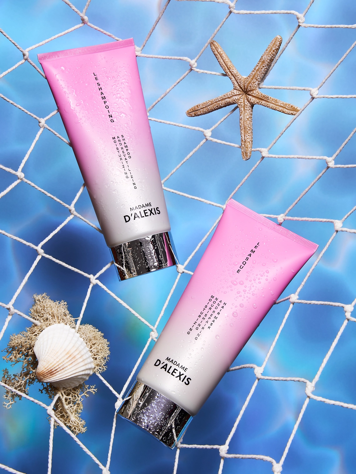 Photographie d'un tube de shampooing et d'un tube de masque capillaire. Ces deux produits sont dans un filet de peche comme si ils venaient d etre peches dans la mer. Les tubes sont rose et blanc. Dans ce filet on voit egalement une etoile de mer, un coquillage et de la mousse, rendant la composition plus realiste, comme si ca venait des fonds marins. En arriere-plan, derriere le filet on voit l'eau de mer. Ambiance estivale, summer, maritime, fraiche, vacances. Le rendu est assez contraste et original - Photographe cosmetiques - photographe publicitaire cosmetiques - photographe produits cosmetiques - Aurore Aivrest