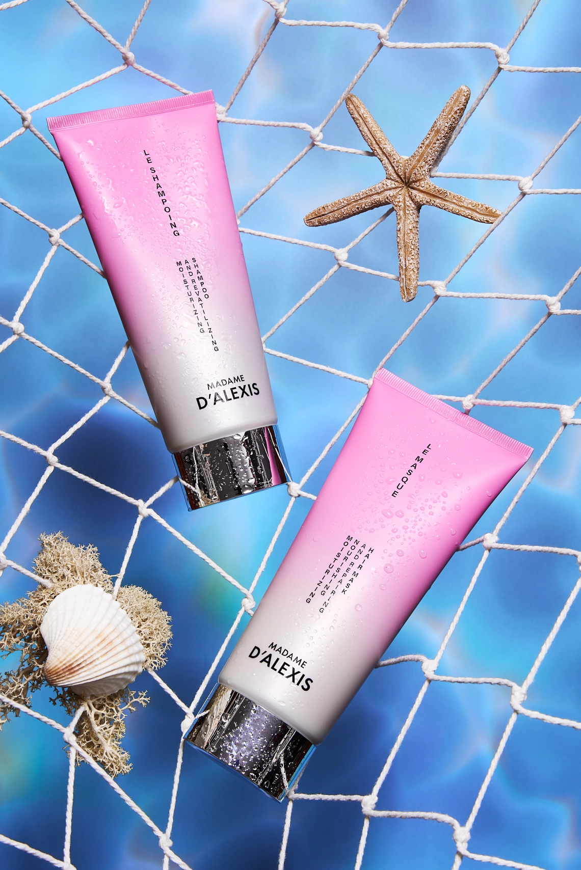 Photographie d'un tube de shampooing et d'un tube de masque capillaire. Ces deux produits sont dans un filet de peche comme si ils venaient d etre peches dans la mer. Les tubes sont rose et blanc. Dans ce filet on voit egalement une etoile de mer, un coquillage et de la mousse, rendant la composition plus realiste, comme si ca venait des fonds marins. En arriere-plan, derriere le filet on voit l'eau de mer. Ambiance estivale, summer, maritime, fraiche, vacances. Le rendu est assez contraste et original - Photographe cosmetiques - photographe publicitaire cosmetiques - photographe produits cosmetiques - Aurore Aivrest