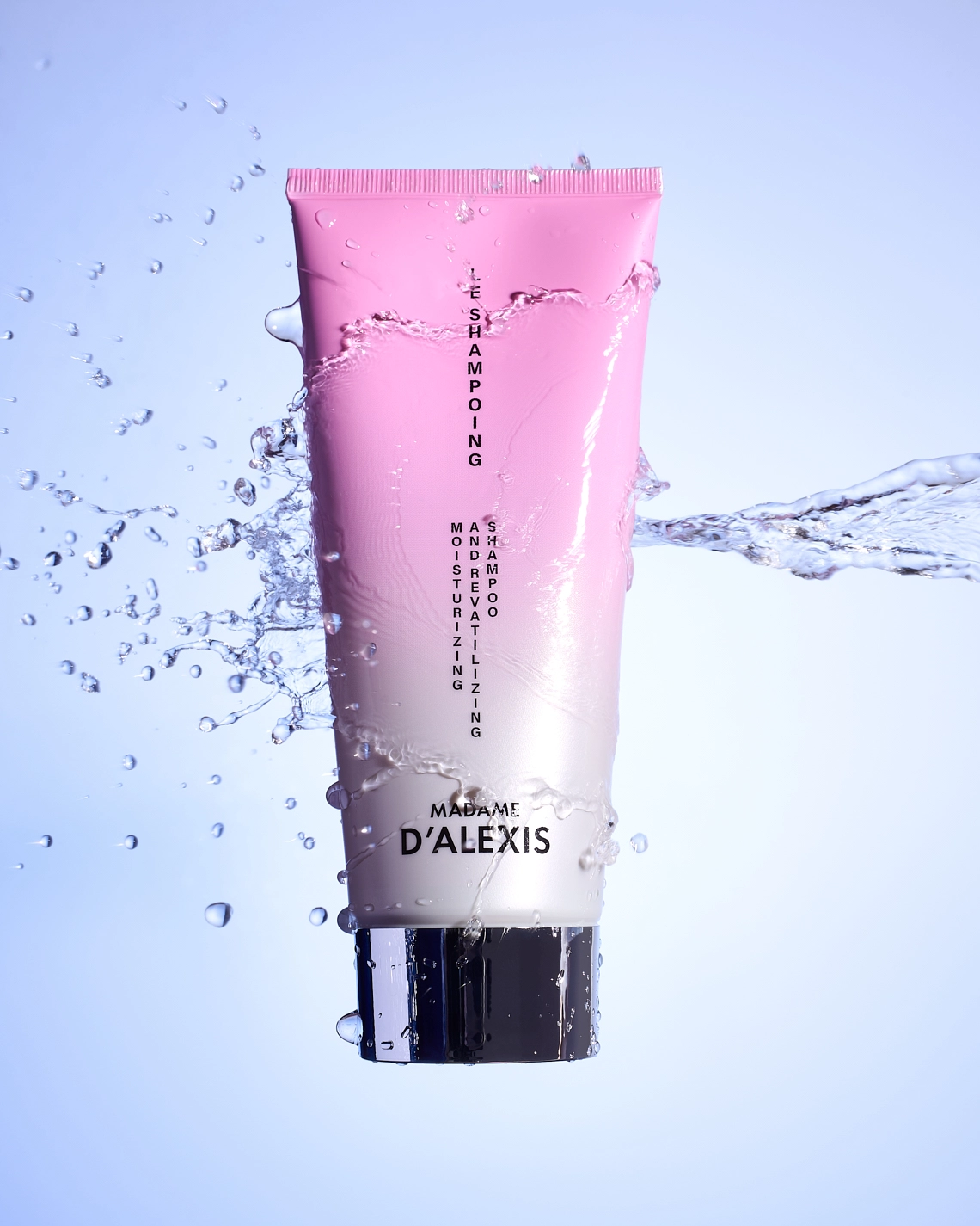 Photographie d'un tube de shampooing rose et blanc, en levitation, qui se fait percuter par un jet d'eau. Le jet d'eau cree des eclaboussures qui enrobent le produit. Le tout est sur un fond bleu ciel pour creer du contraste et apporter la touche de fraicheur. Le rendu est percutant, impactant et dynamique - Photographe cosmetiques - studio photo cosmetiques - photographe produits cosmetiques - Aurore Aivrest