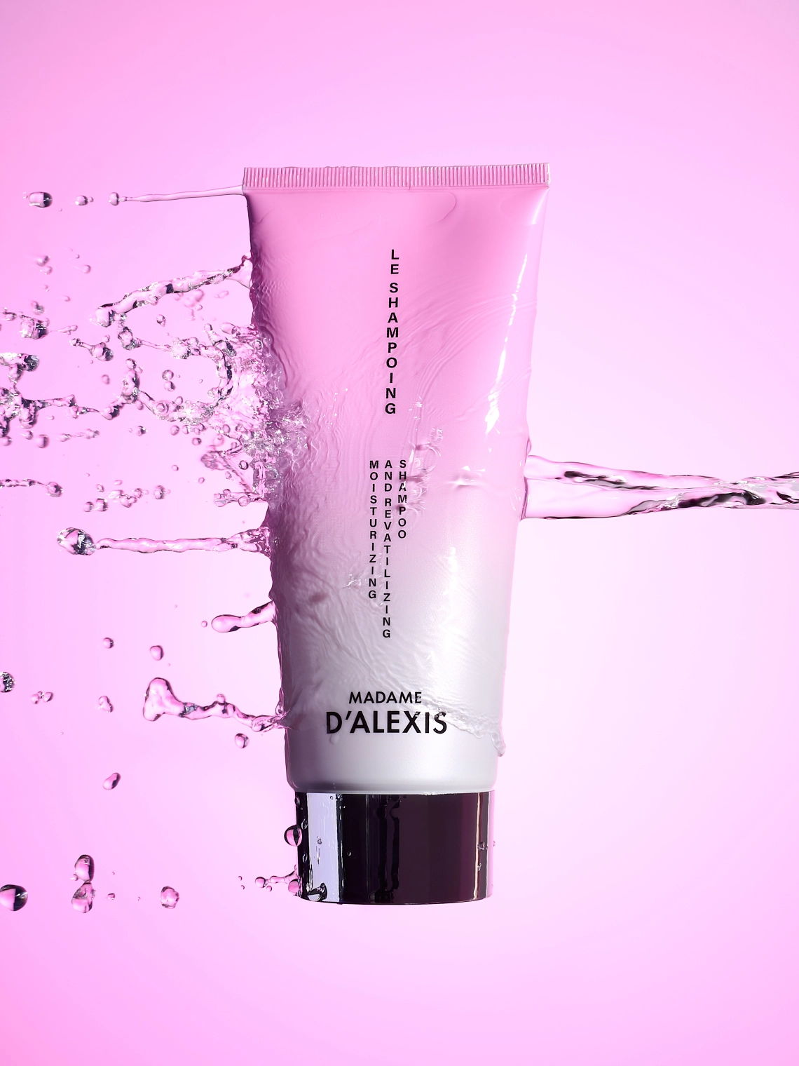 Photographie d'un tube de shampooing rose et blanc, en levitation, qui se fait percuter par un jet d'eau. Le jet d'eau cree des eclaboussures qui scintillent avec la lumiere. Le tout est sur un fond rose pour evoquer la feminite. Le rendu est delicat, scintillant et dynamique - Photographe cosmetiques - studio photo cosmetiques - photographe publicitaire cosmetiques - Aurore Aivrest
