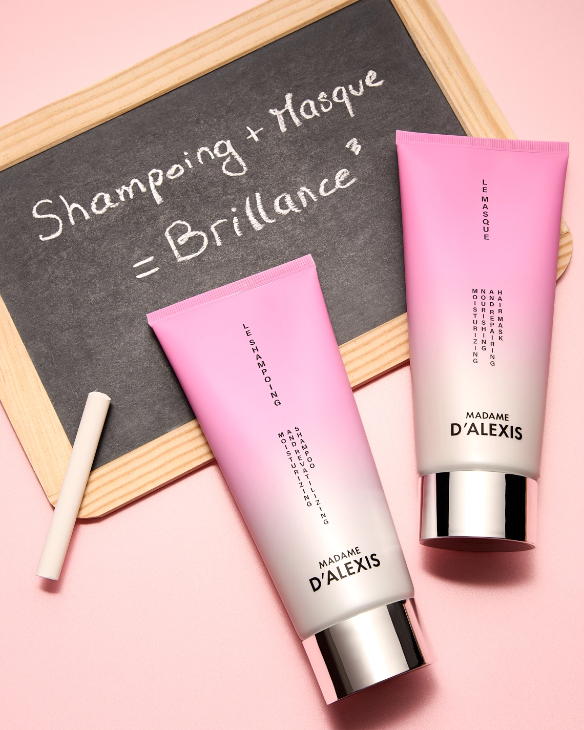 Photographie de deux tubes de produits capillaires, un shampoing et un masque. Ils sont rose et blanc. Ils sont couches sur une ardoise d'ecole. Il y a aussi une craie blanche posee sur le coin gauche de l'ardoise. Une equation est inscrite sur cette ardoise. Le tout sur un fond rose clair. Ambiance scolaire, rentree, reprise du travail, fin des vacances, retour a l'ecole. Le rendu est assez luxueux - Photographe cosmetiques - photographe publicitaire cosmetiques - photographe produits cosmetiques - Aurore Aivrest