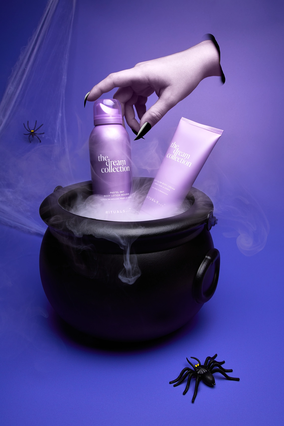 Photographie de deux produits cosmetiques dans une mise en scene sur le theme d'halloweeen, dans une ambiance froide, classe, violet et noir. Avec araignees, toile d'araignees, chaudron avec fumee et main de sorciere coupee volante - Photographe cosmetiques - photographe still life cosmetiques - photographe produits cosmetiques - Aurore Aivrest