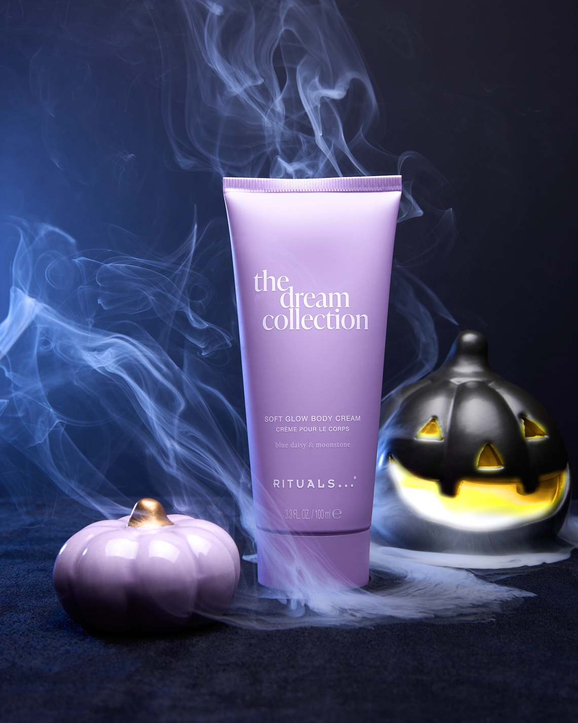 Photographie d un tube de creme pour le corps violet dans une mise en scene sur le theme d'halloweeen, dans une ambiance froide, vaporeuse, fumante, classe, violet, bleu et noir. Avec citrouille violette, citrouille noire illuminee et fumee - Photographe cosmetiques - photographe still life cosmetiques - photographe produits cosmetiques - Aurore Aivrest